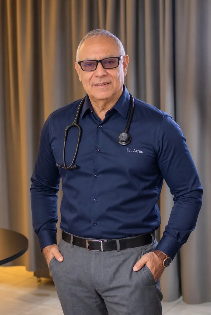 El Dr. Heriberto Arras con camisa azul bordada y estetoscopio en su consultorio